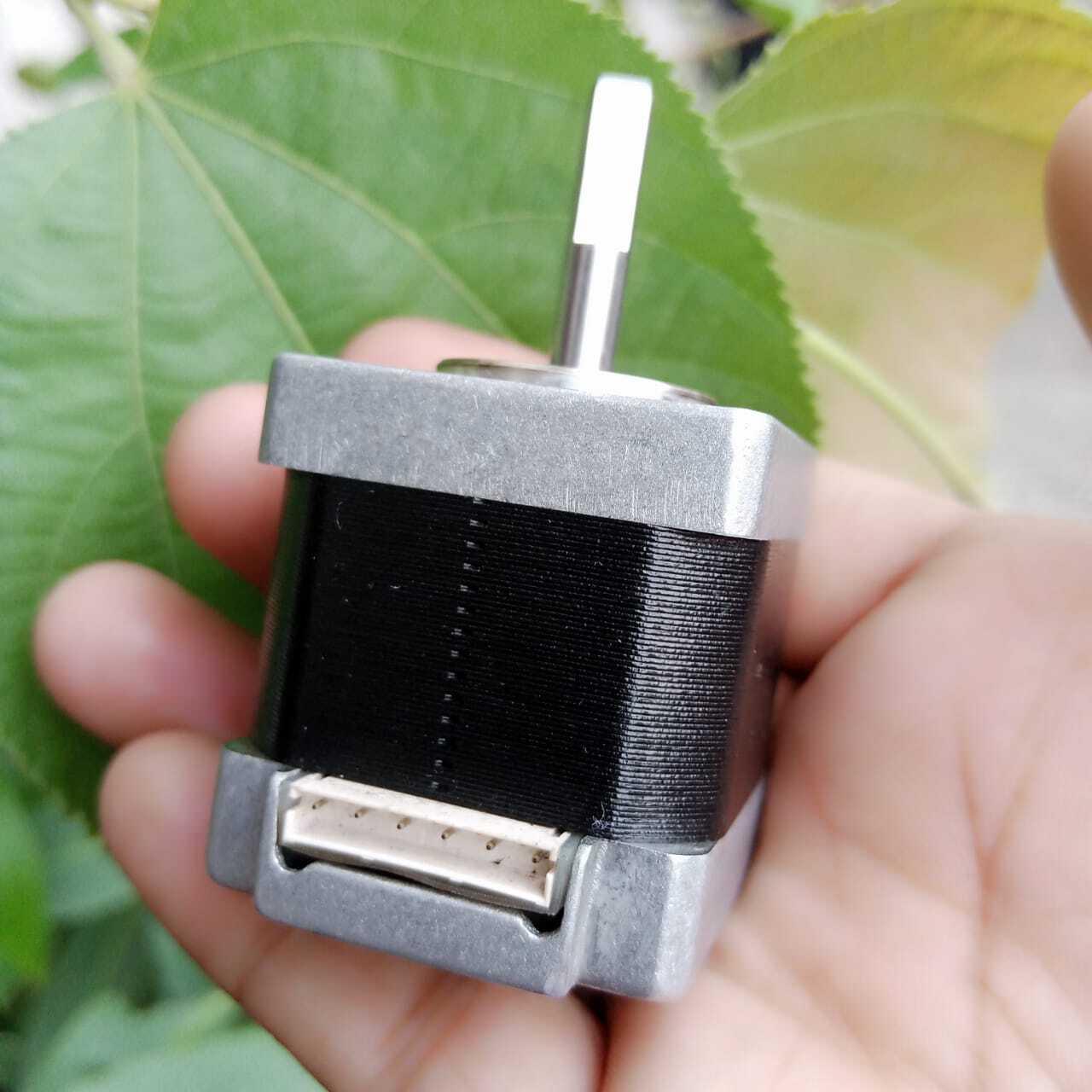 NEMA 11 stepper motor without connector - shown held in a hand, featuring a black cylindrical body, silver metal ends, a vertical metal shaft, and a white connector port.
