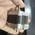 NEMA 17 Stepper Motor Dual Shaft Model B-2381715B - shown held in a hand, featuring a black square body, silver end caps, dual shafts, and a white connector.