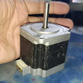NEMA 23 Stepper Motor In Pakistan (1.5A–2.0A, 1.8°) - a square silver and black motor with a protruding metal shaft and a white electrical connector port on the side.