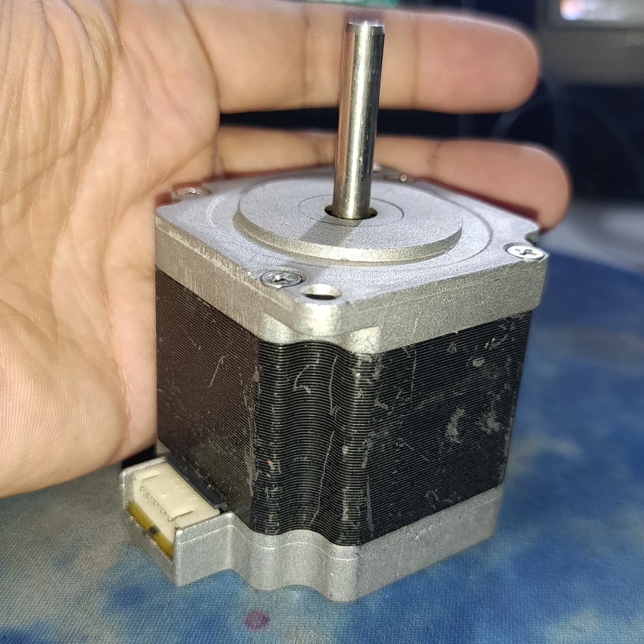 NEMA 23 Stepper Motor In Pakistan (1.5A–2.0A, 1.8°) - a square silver and black motor with a protruding metal shaft and a white electrical connector port on the side.