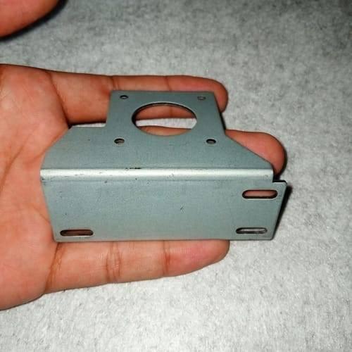 NEMA17 Stepper Motor Mounting Bracket NEMA17 Fitting - a grey L-shaped metal bracket with a circular center hole and four mounting slots, held in a hand.