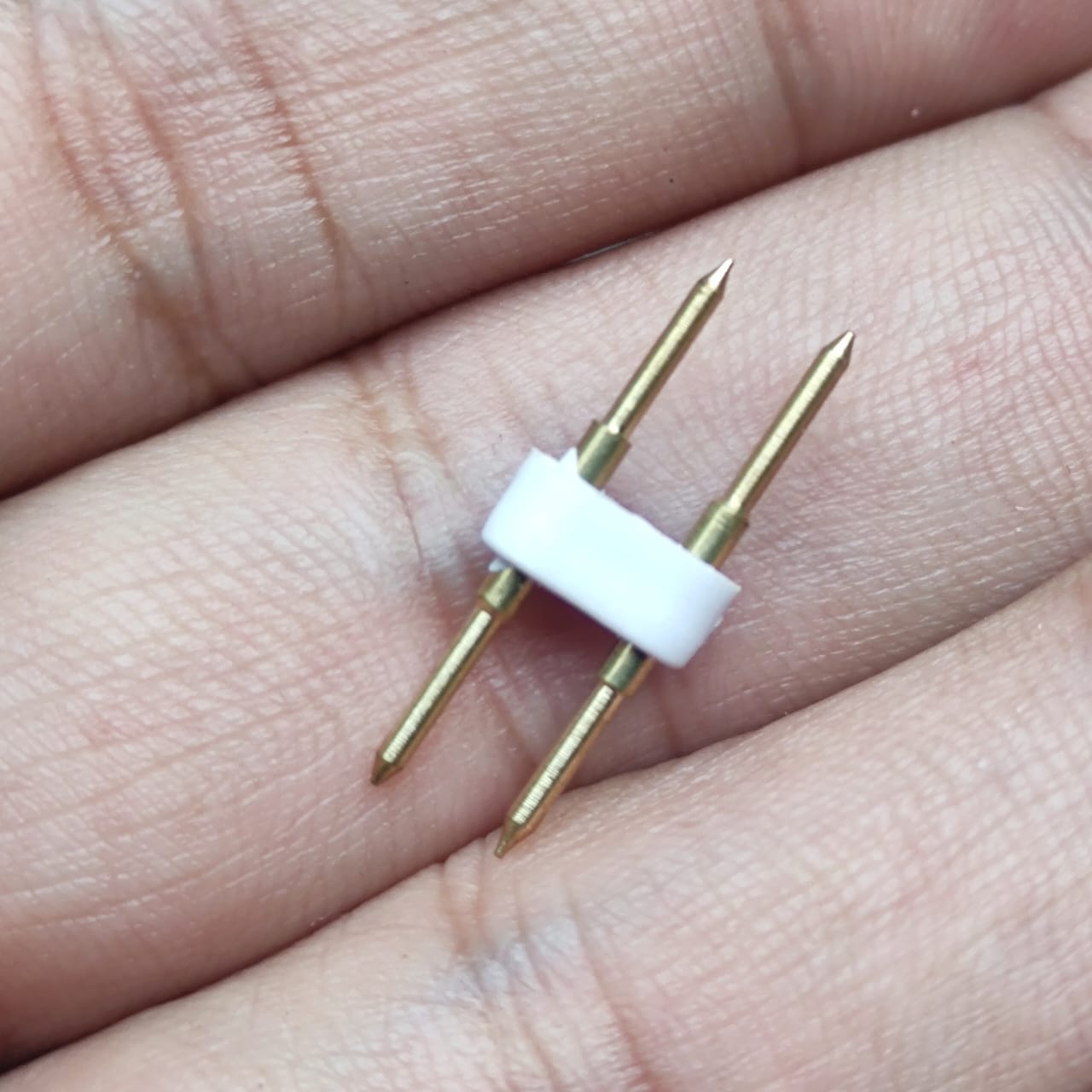 Neon Light Connector Pin - a close-up of a small white plastic piece holding two parallel gold-coloured metal pins being held by fingers.
