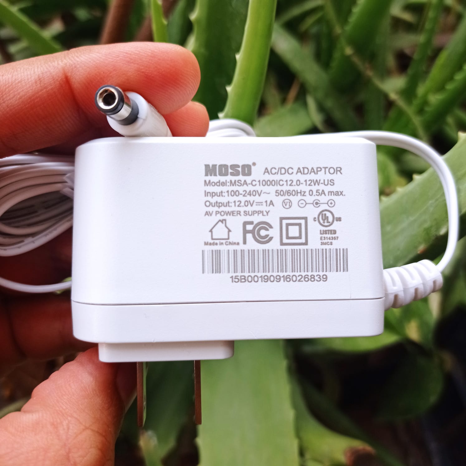 New High Quality 220V To 12V 1A AC DC Adapter - a white wall-plug power supply with a barrel connector, showing technical specifications printed on its body.