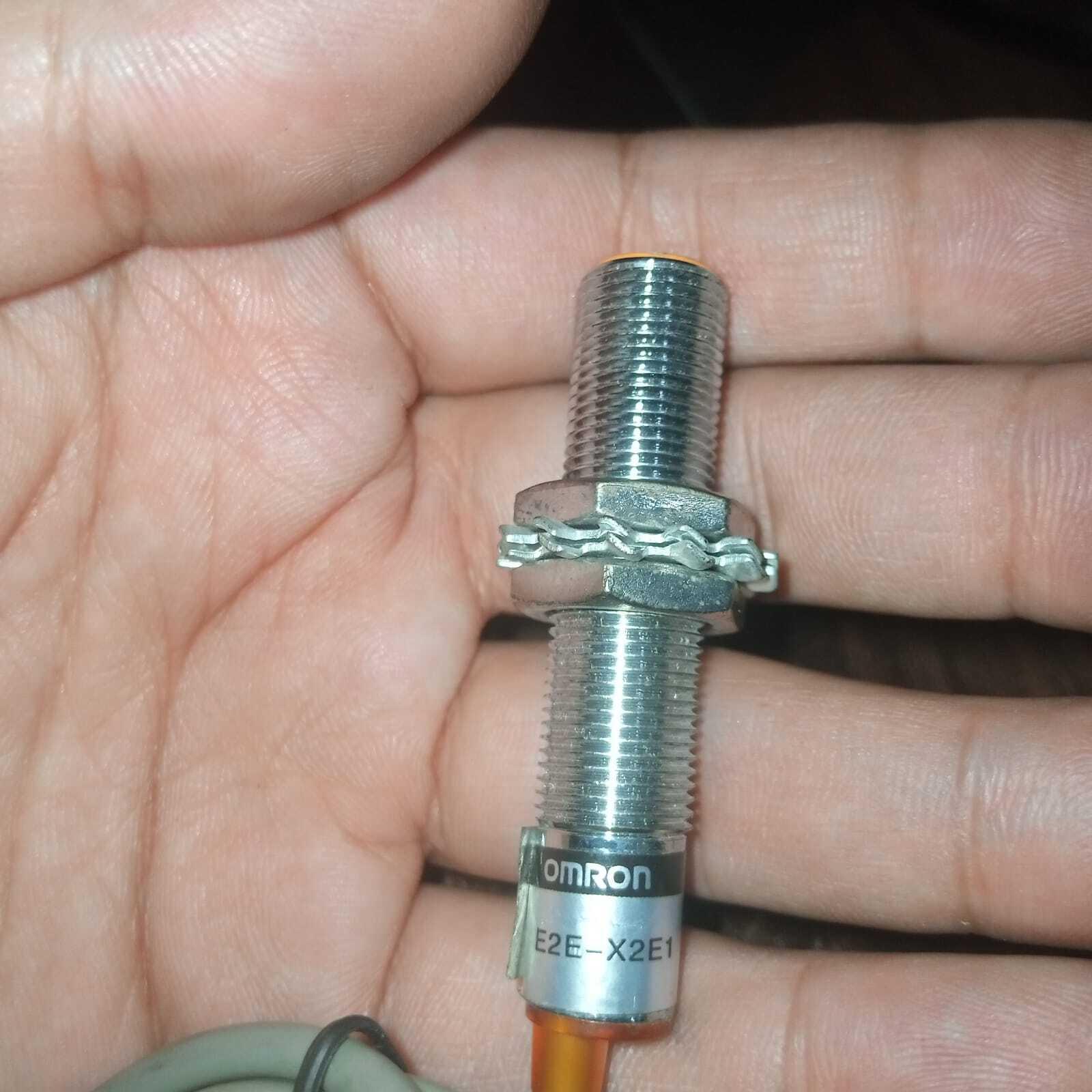 Omron Inductive Proximity Sensor Switch E2e-X2E1 - a cylindrical silver metal sensor with a threaded body, two nuts, and a washer held in a hand.