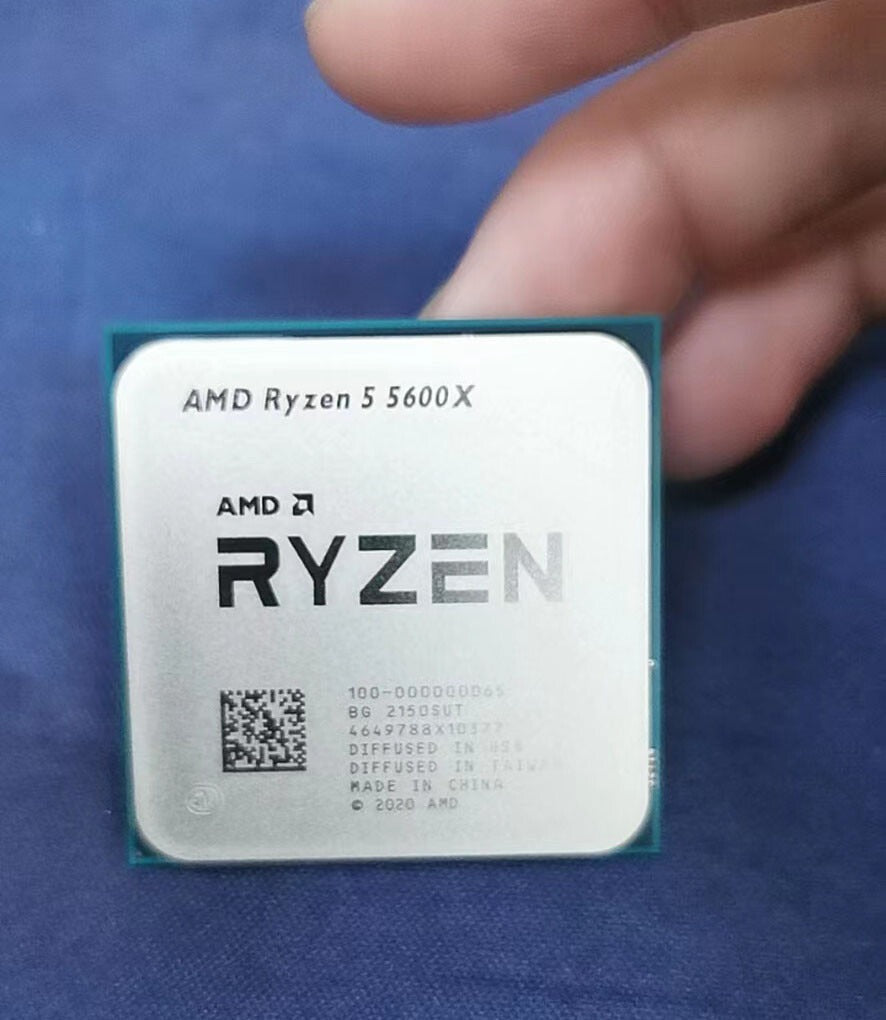 On Demand AMD Ryzen 5 5600X CPU - 6 Cores, 4.6 GHz Boost AM4 Socket - a square silver-topped processor held by fingers, showing laser-etched branding and technical text on its metal heat spreader.
