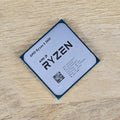On-Demand AMD Ryzen R5 3600 Processor | 6-Core 12-Thread CPU for Gaming And Work - a square silver-topped CPU with black text and a QR code, resting on a light-colored wooden surface.