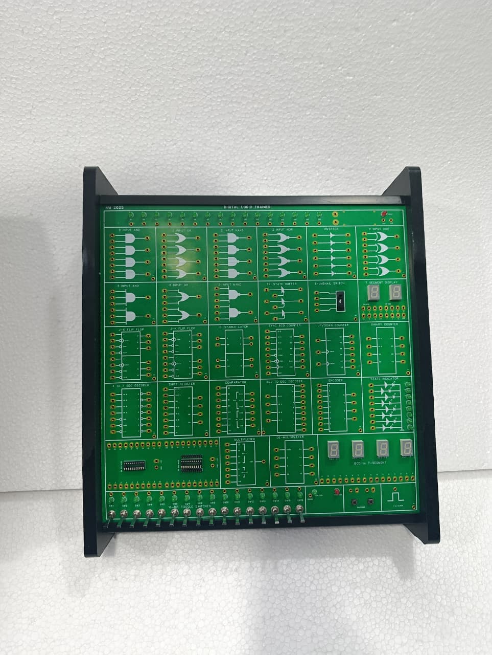On Demand DLD Trainer Digital Logic Trainer WWW.DIGILOG.PK - a green, rectangular circuit board featuring various logic gates, toggle switches, and LED displays.