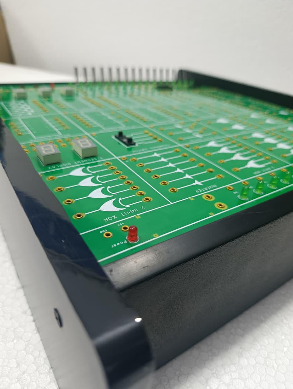 On Demand DLD Trainer Digital Logic Trainer WWW.DIGILOG.PK - a green circuit board with logic gate symbols, two 7-segment displays, and a red power indicator LED.
