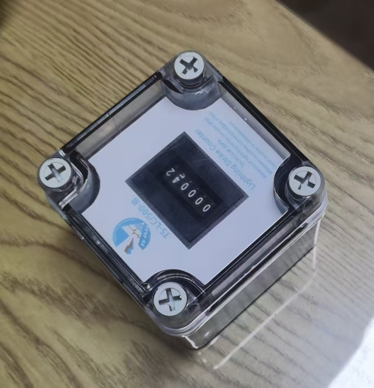 On-Demand LIGHTNING STRIKE COUNTER - TS-LC/500-III, a square device with a clear plastic cover, four corner screws, and a digital display reading 000042.