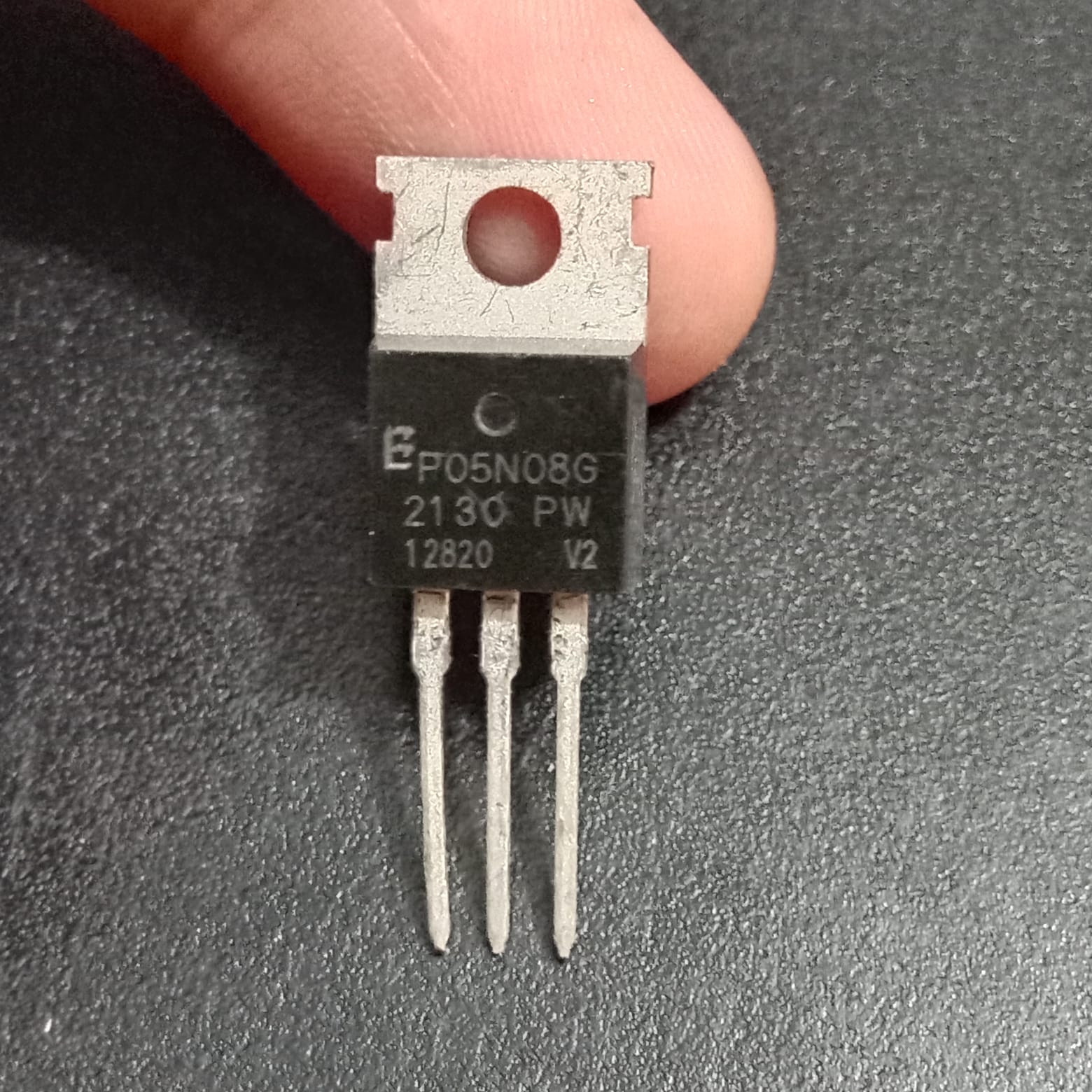P05N08G 80V 120A TO 20N Channel Enhanced Power MOSFET - a black three-pin electronic component in a TO-220 package with a metal mounting tab, held by a finger against a dark background.