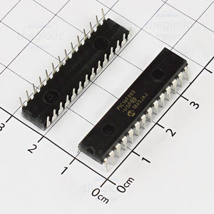 PIC16F883 IC Microcontroller PRICE - two black 28-pin dual in-line package integrated circuits placed on a white grid surface for scale.
