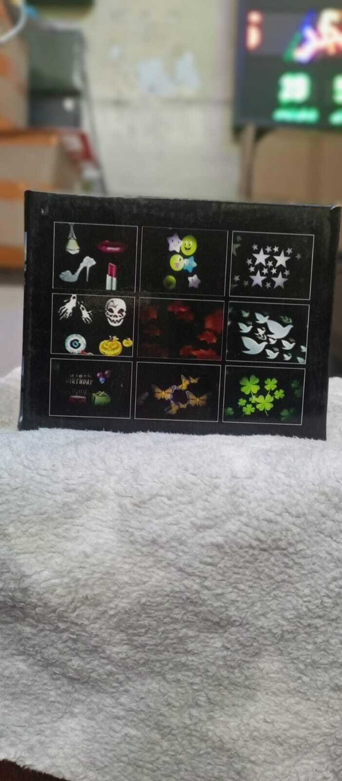 Projector - Projector packaging box showing a grid of nine different light projection patterns, including stars, butterflies, clovers, and birthday themes.