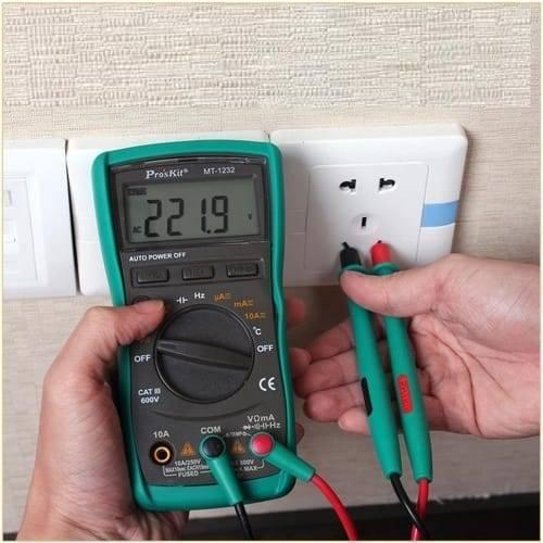 Proskit Autorange Digital Multimeter Mt 1232 For AC DC Voltage Current Resistance Temperature Measurement Tester - a green handheld unit with a digital display reading 221.9 AC and probes testing a wall outlet.