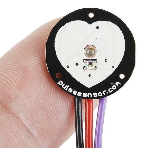 Pulse Sensor Pulse Heart Rate Sensor Arduino Heartbeat Sensor - a close-up of the circular heart-shaped black and white PCB held by fingers with three attached red, black, and purple wires.
