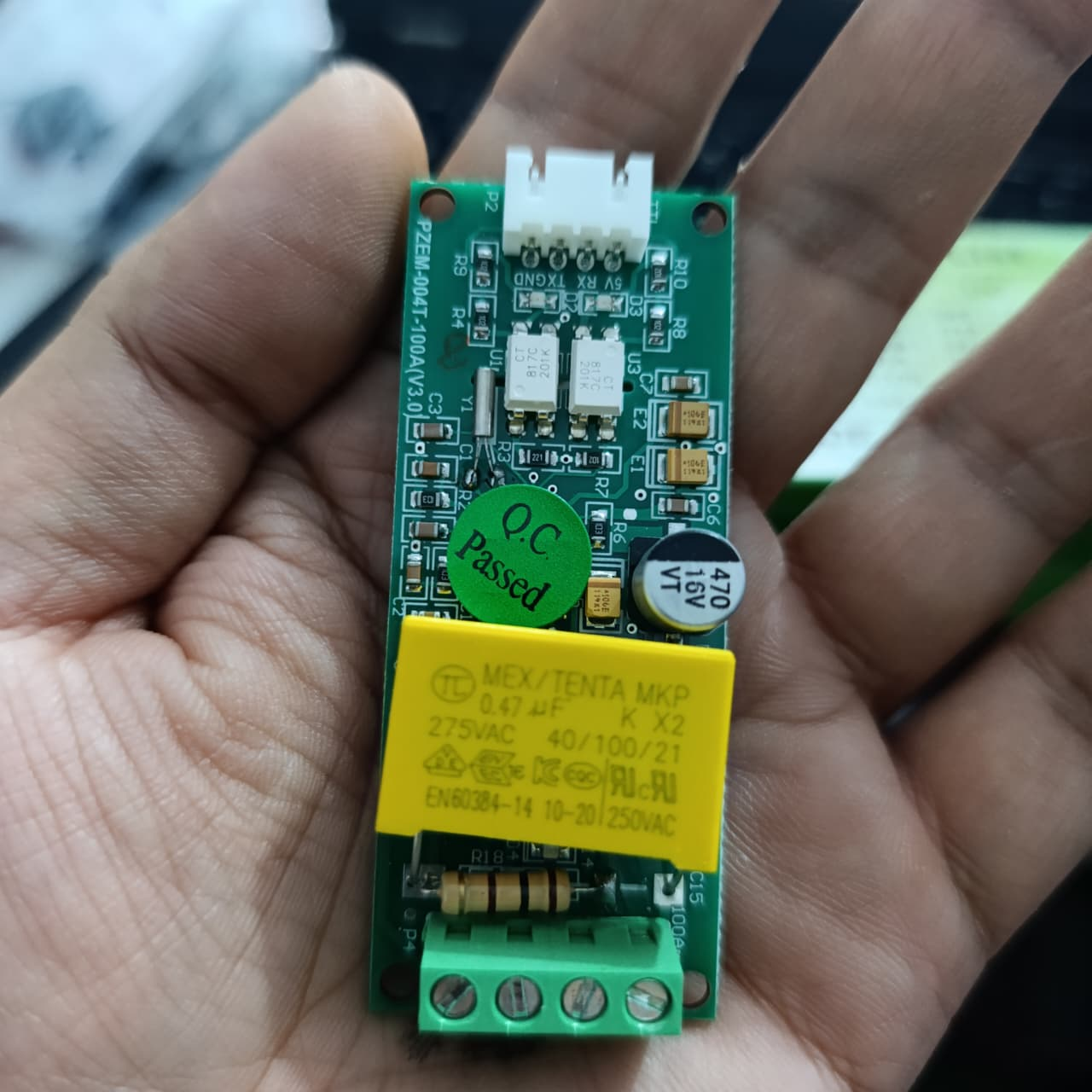 PZEM-004T 100A Single Phase Power Energy Meter Module - held in a hand, showing a green circuit board with a yellow capacitor, a four-pin terminal block, and a white connector port.