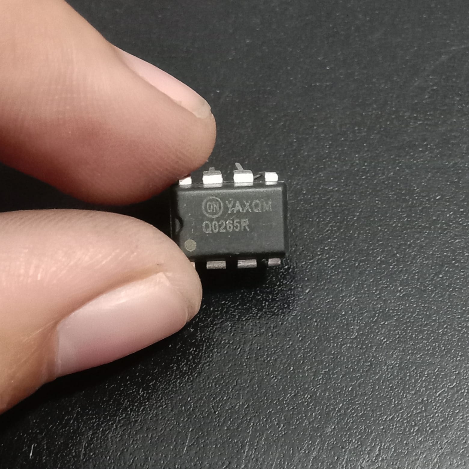 Q0265R High-Voltage Switcher for Offline SMPS IC Used - a close-up of a black, rectangular 8-pin integrated circuit held by fingers, showing the ON Semiconductor logo and text.