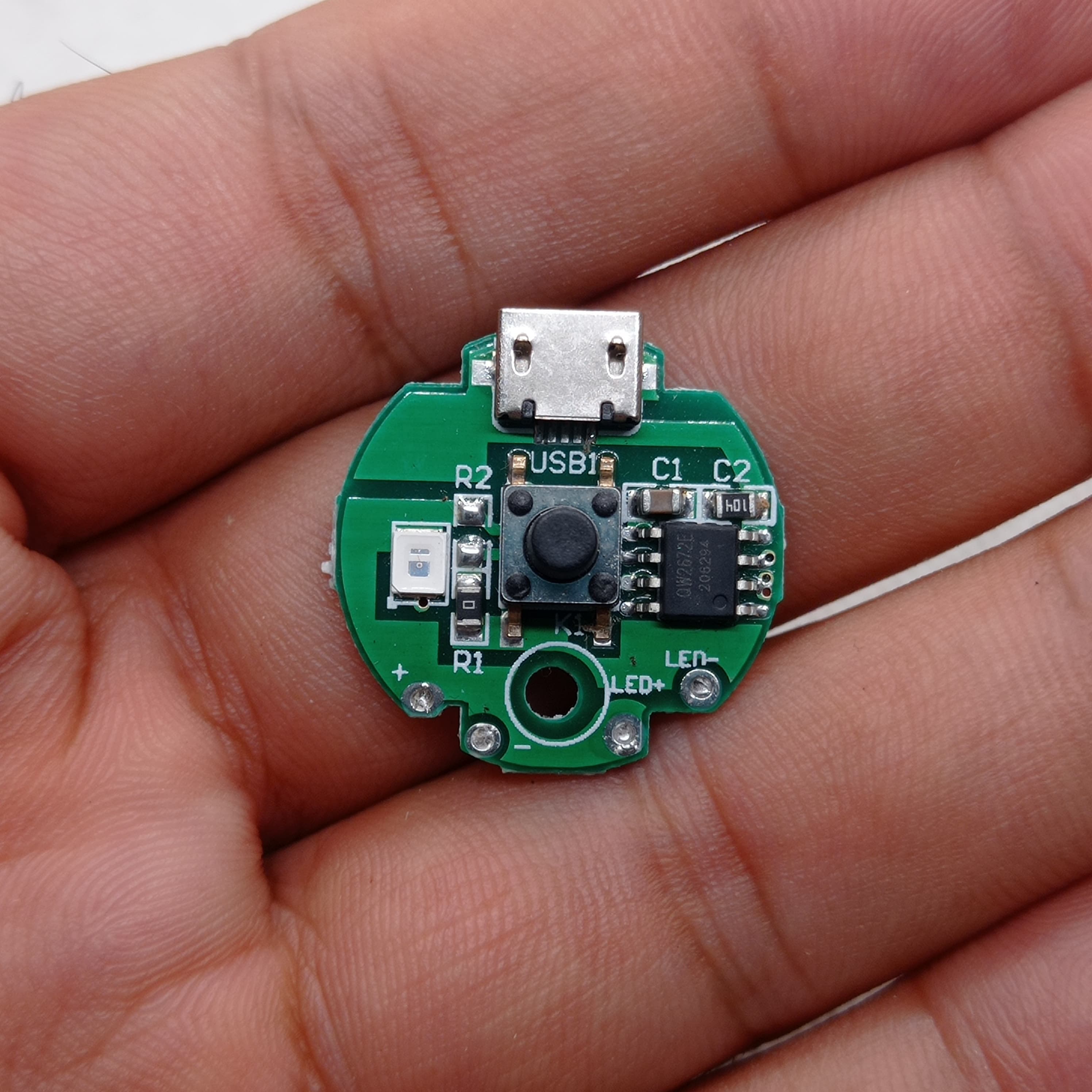QW2672 Torch Light Emergency Light Controller Module - a circular green PCB held in a hand, featuring a micro-USB port, a push-button, and an LED.