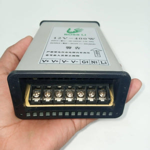 Rainproof 400W 12V 33A Switching Power Supply Driver - shown held in a hand, featuring a silver metal casing with terminal screw connectors and a label.