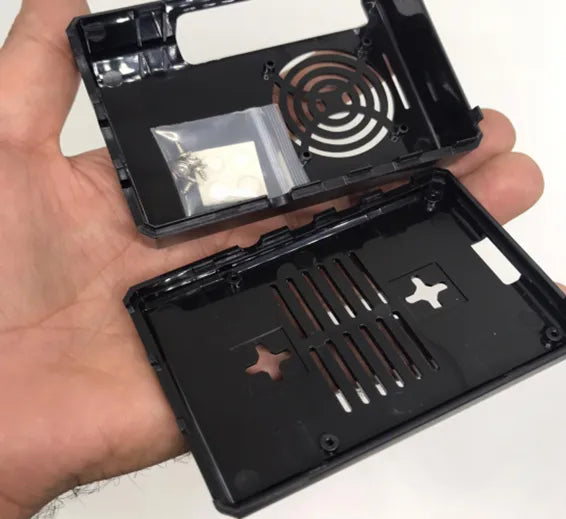 Raspberry Pi 4 Casing With Fan Fitting Camera Cable Port and GPIO Port - shown as two black plastic housing pieces with included screws and adhesive pads.