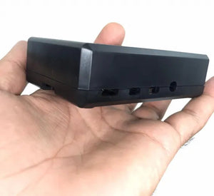 Raspberry Pi 4 Casing With Fan Fitting Camera Cable Port and GPIO Port - shown in a hand, featuring a black plastic rectangular enclosure with side ports.