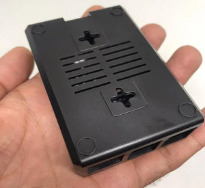 Raspberry Pi 4 Casing With Fan Fitting Camera Cable Port and GPIO Port - black plastic enclosure held in a hand, showing the bottom, vents, and screw holes.