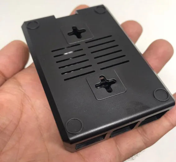 Raspberry Pi 4 Casing With Fan Fitting Camera Cable Port and GPIO Port - black plastic enclosure held in a hand, showing the bottom, vents, and screw holes.