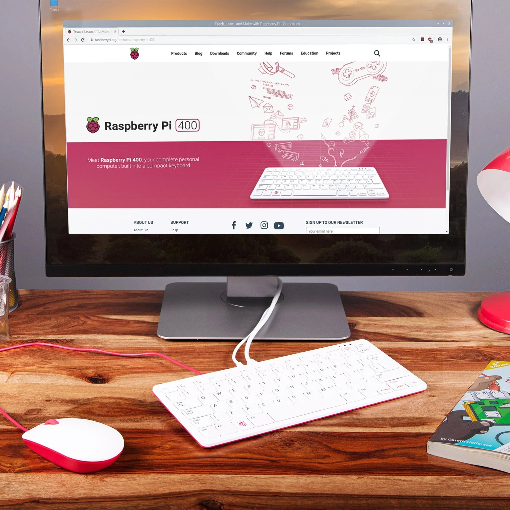 Raspberry Pi 400 4GB RAM Your Complete Personal Computer, Built Into a Compact Keyboard-digilog.pk - a white and red compact keyboard computer connected to a monitor displaying the Raspberry Pi website, with a matching mouse.