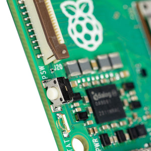 Raspberry Pi 5 4GB - a close-up of the green circuit board showing the white power button, a brown ribbon cable connector, and a Dialog chip.
