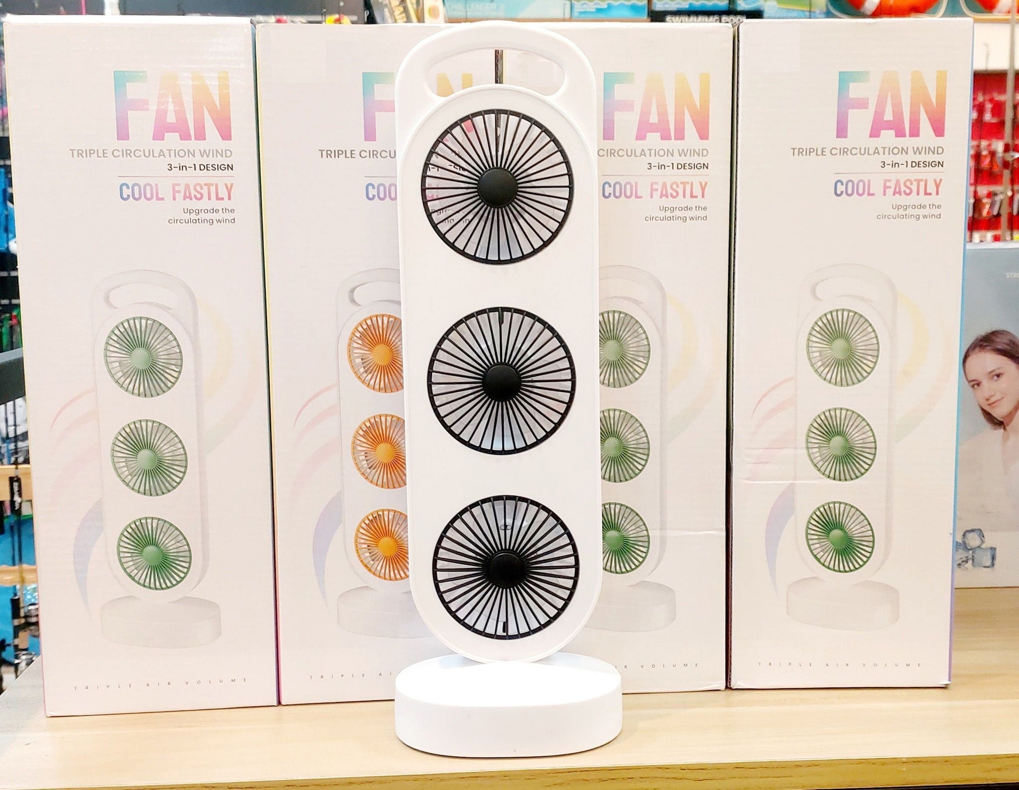 Rechargeable Triple Circulation Wind Fan price - shown as a white, vertical, three-fan unit standing in front of four identical product boxes on a shelf.