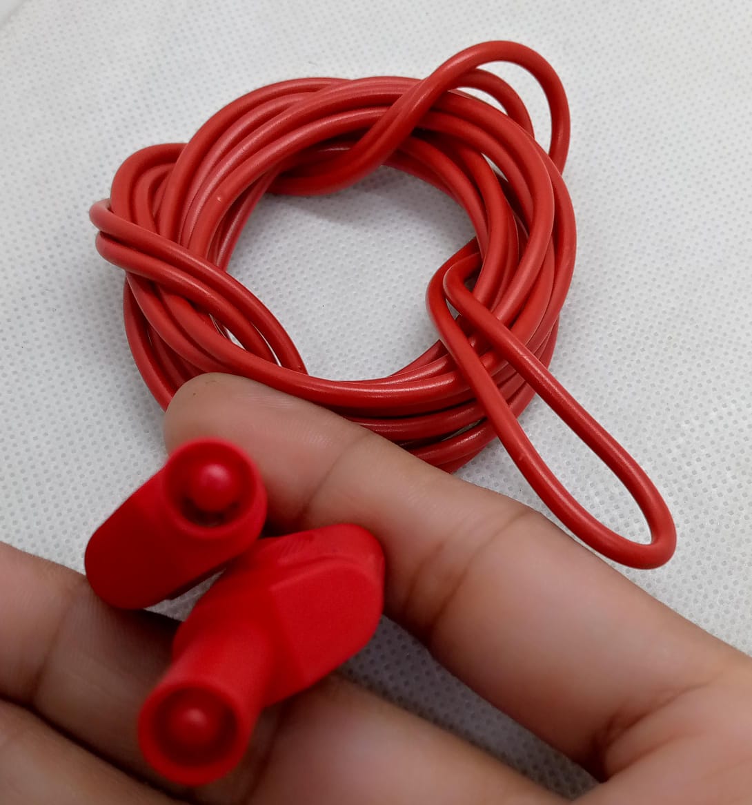 Red Banana Clip Wires 2 Meter | High-Quality Test Leads | Digilog.pk - a close-up of two red banana plug connectors held in a hand with the attached red electrical wire coiled behind.