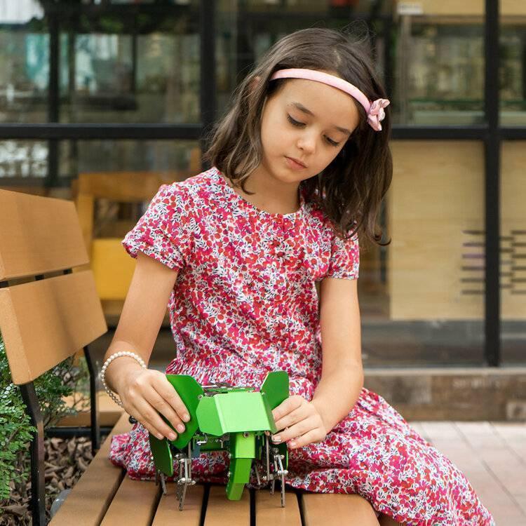 Robobloq Q-elephant Robot Kit - shown as a green, elephant-shaped metal robot being held by a young girl sitting on a wooden bench.