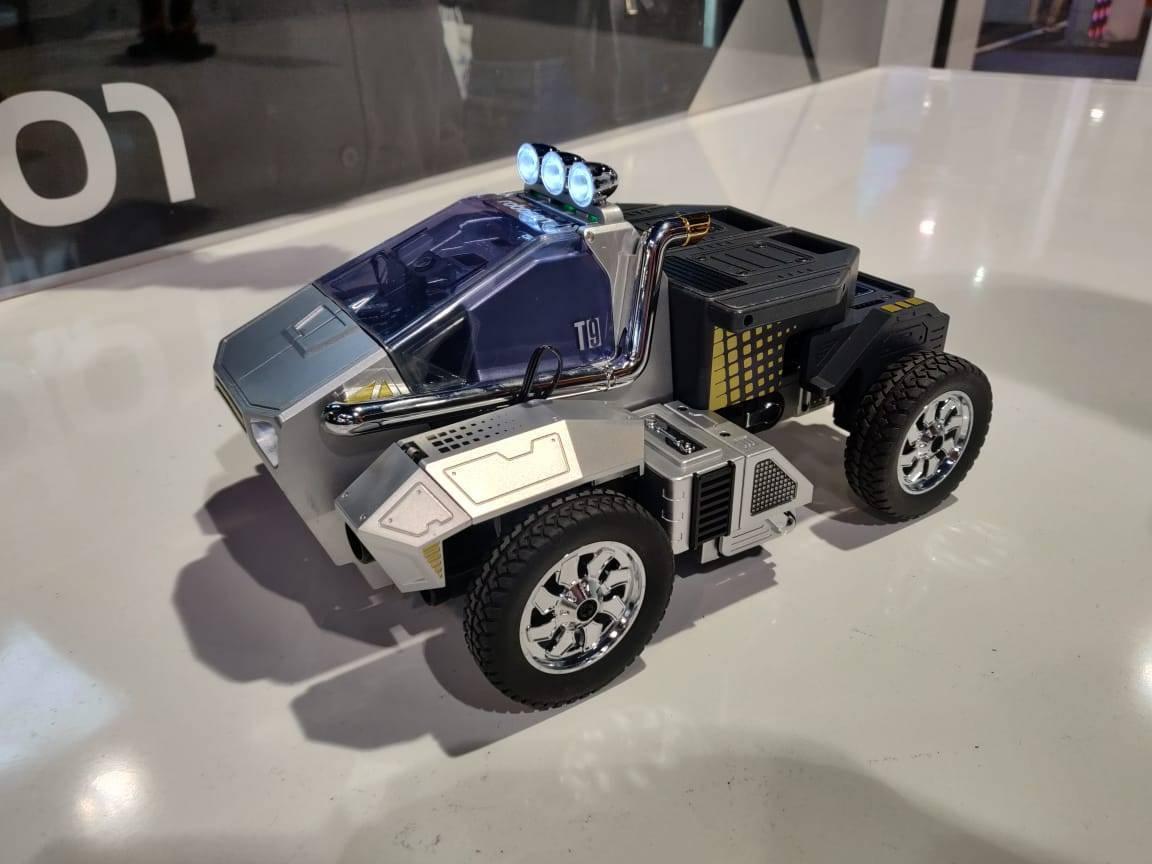Robosen T9 - Advanced Programmable And Convertible Robot - STEM: Fun, Educational With Voice And App Control - a silver and black programmable robot toy in vehicle mode, featuring chrome wheels, a blue cockpit, and three illuminated roof lights.