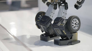 Robosen T9 - Advanced Programmable And Convertible Robot - STEM: Fun, Educational With Voice And App Control - a close-up of the black and silver robotic legs featuring visible wheels, mechanical joints, and textured foot panels on a white surface.