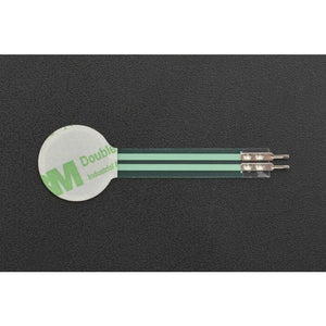 RP-C18.3-LT Thin Film Pressure Sensor - a circular white adhesive pad connected to a flat green ribbon cable with two metal pin connectors at the end.