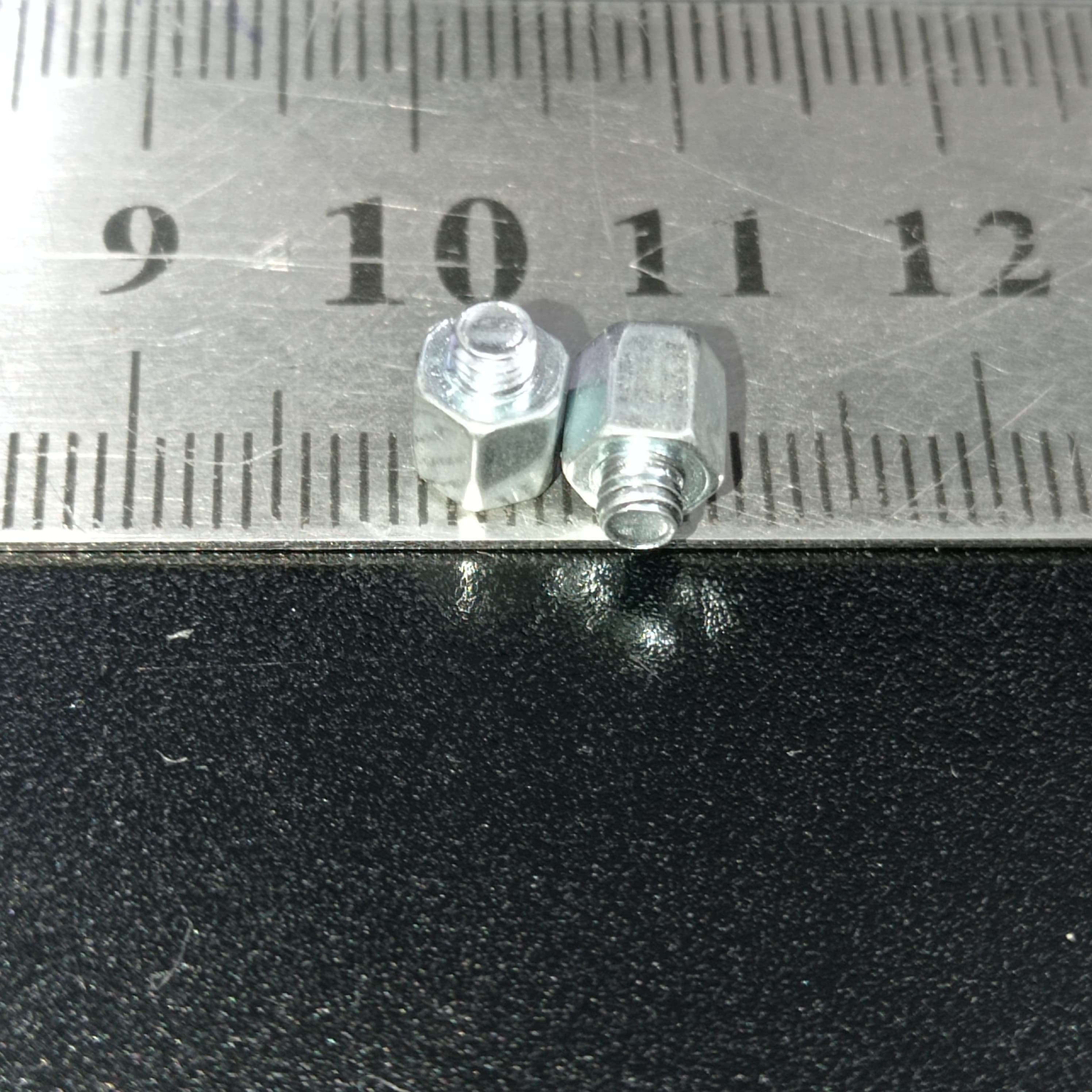 Screw Standoffs Spacers M3 Male x M3 Female - shown in a close-up view next to a metal ruler to indicate their size.