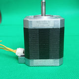 Shinano Kenshi STP-42D4042 2A 1.8 Degree Per Step 0.53nm Stepper Motor - a silver and black cylindrical unit with a metal shaft, featuring a white connector with yellow wires on a green background.