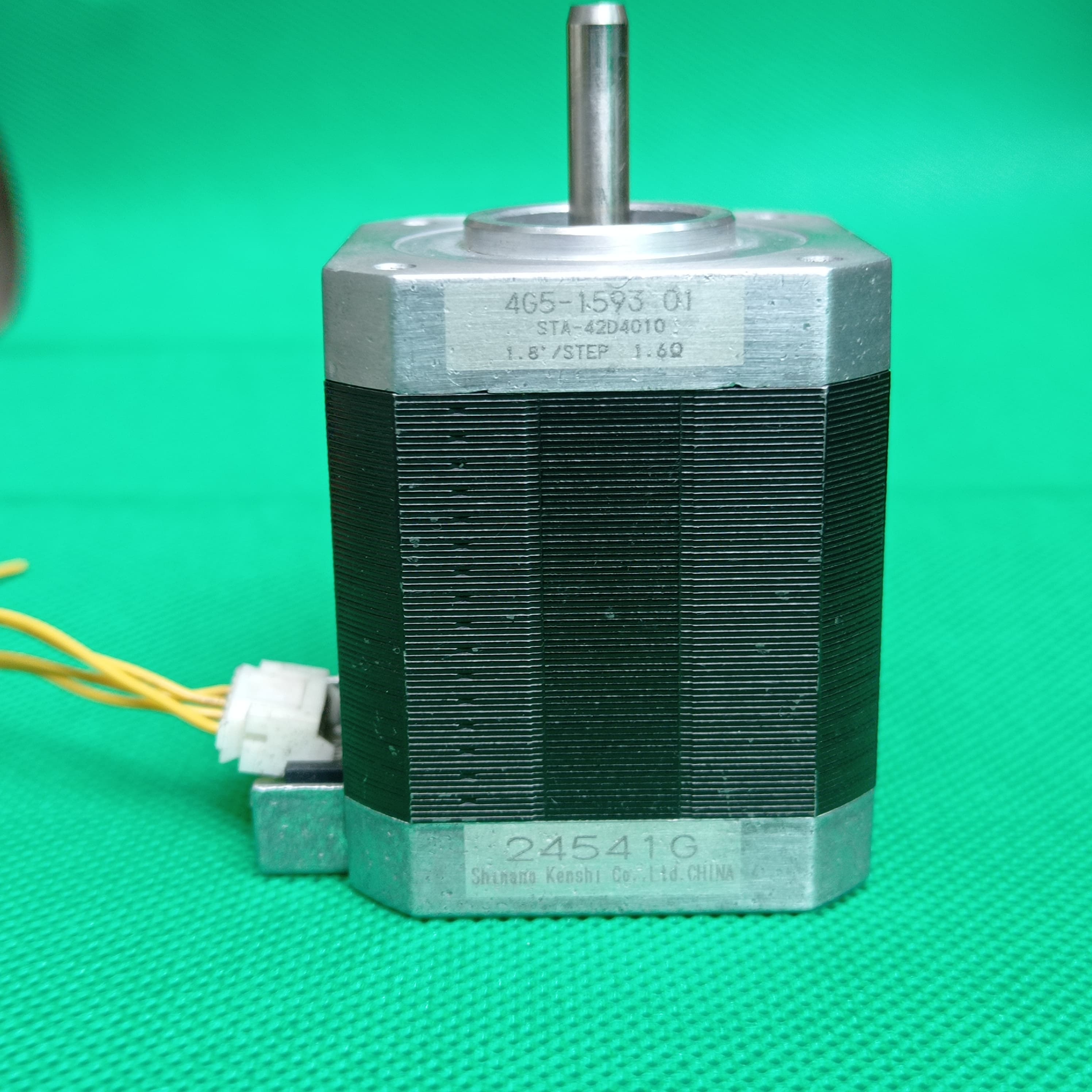 Shinano Kenshi STP-42D4042 2A 1.8 Degree Per Step 0.53nm Stepper Motor - a silver and black cylindrical unit with a metal shaft, featuring a white connector with yellow wires on a green background.