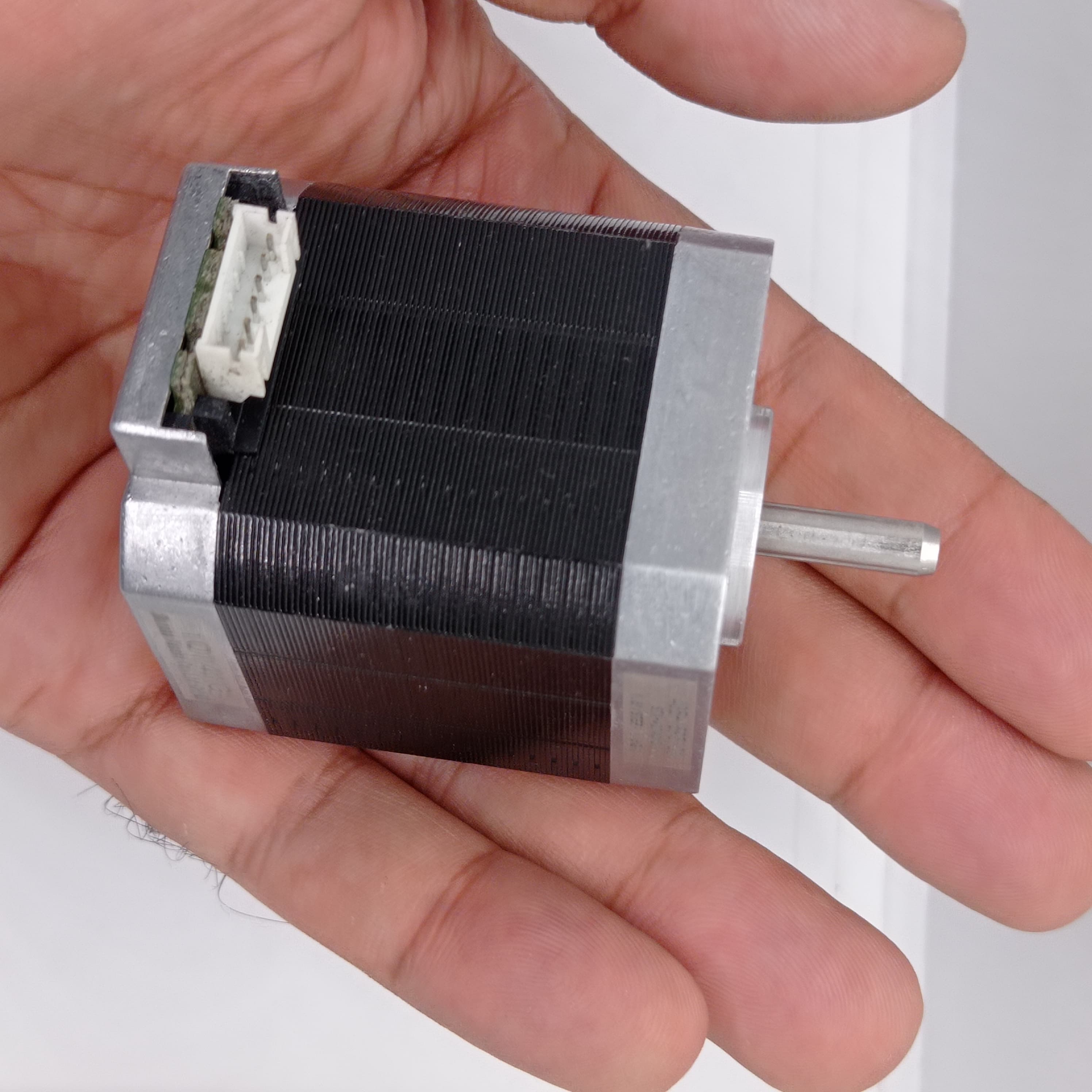 Shinano Kenshi STP-42D4042 2A 1.8 Degree Per Step 0.53nm Stepper Motor - its black square body, silver metal ends, a rotating shaft, and a white electrical connector.