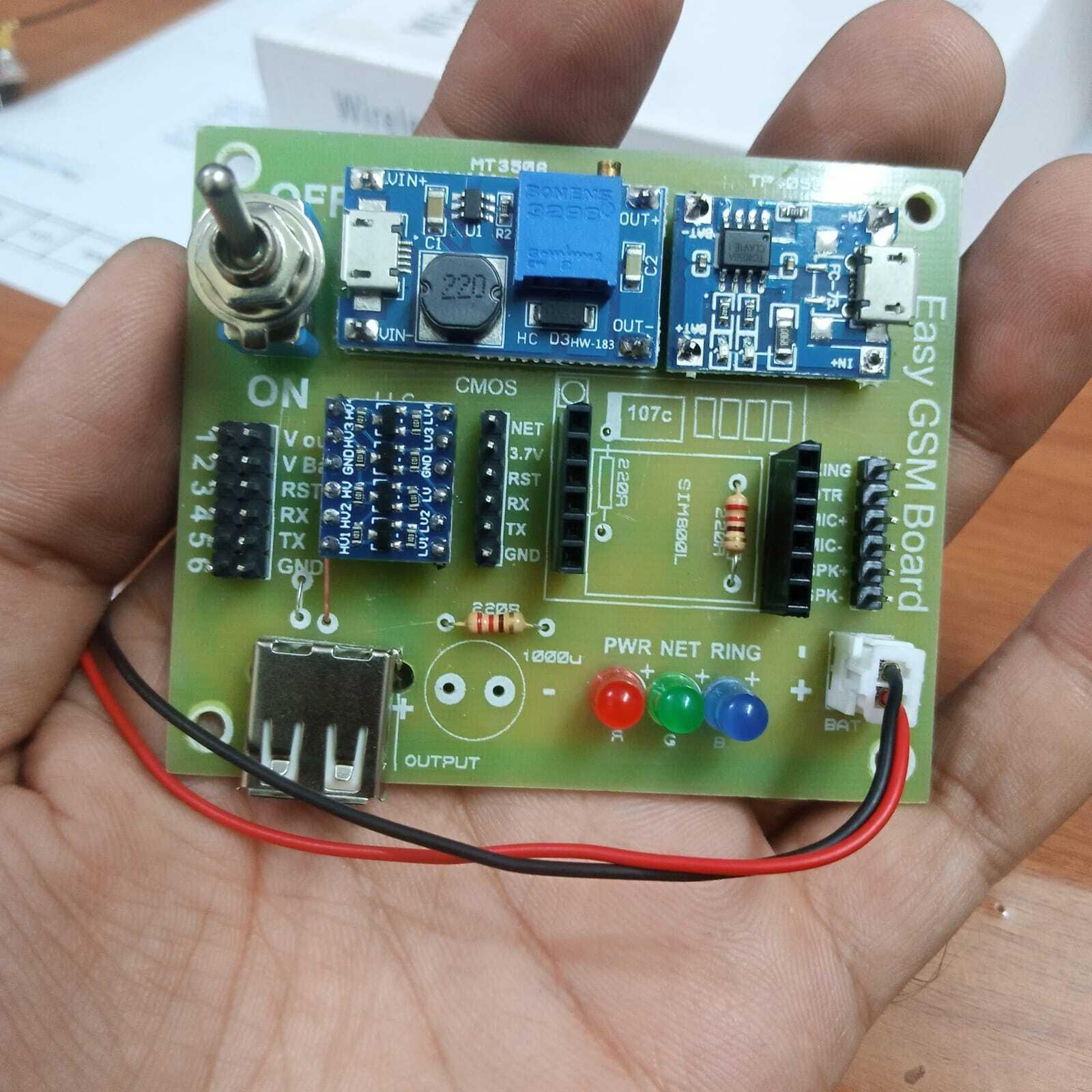 SIM800L Easy GSM Board GSM Breakout Board With Battery SIM800L GSM Shield - shown held in a hand, featuring a green PCB with a toggle switch, USB port, SIM800L module, indicator LEDs, and battery wires.