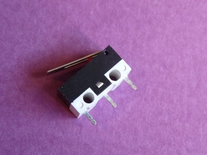Small Microswitch / Limit Switch - shown in a close-up angle, featuring a black and white rectangular body with a metal lever and three metal terminal pins.
