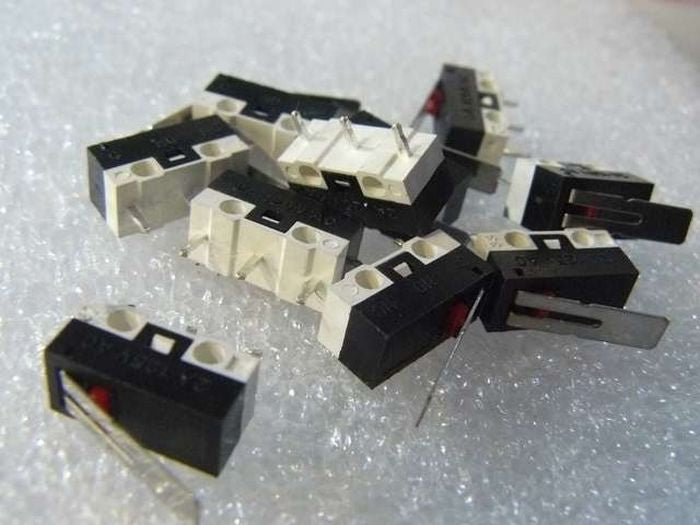 Small Microswitch / Limit Switch - shown as a pile of black and white rectangular switches with red buttons and metal levers on a white textured surface.