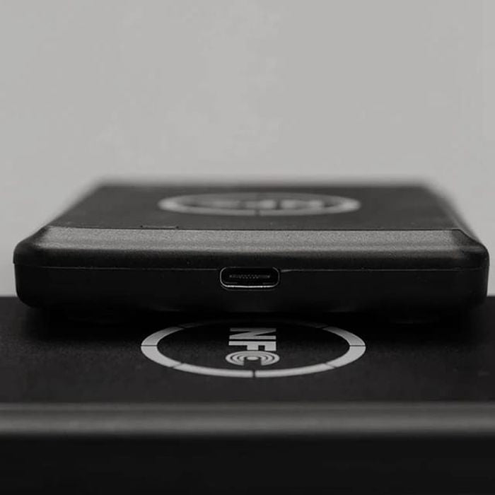 Smart Card Reader AND WRITER Recorder RFID IC Copier, NFC Duplicator, 13.56MHz - a close-up of the black device's side profile with a micro-USB port resting on a surface marked with an NFC logo.