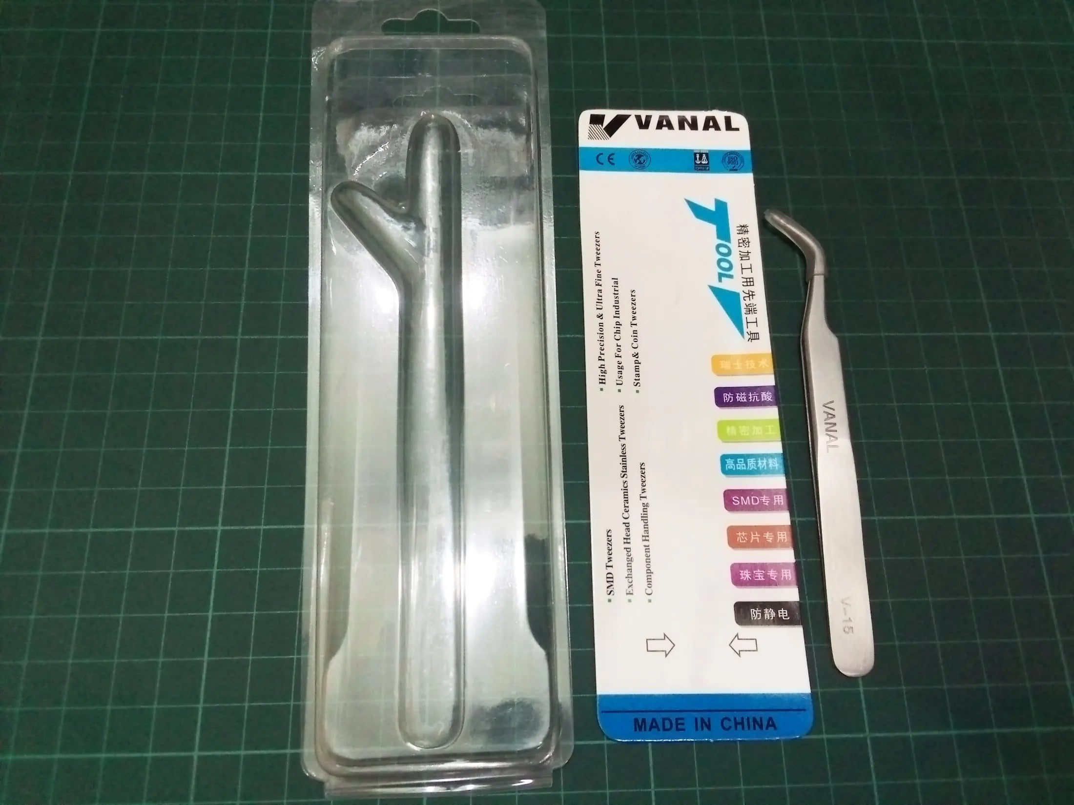 SMD Bend Tweezer VANAL V-15 For Positioning Components - shown with its silver metal body, branded backing card, and empty clear plastic packaging on a green cutting mat.