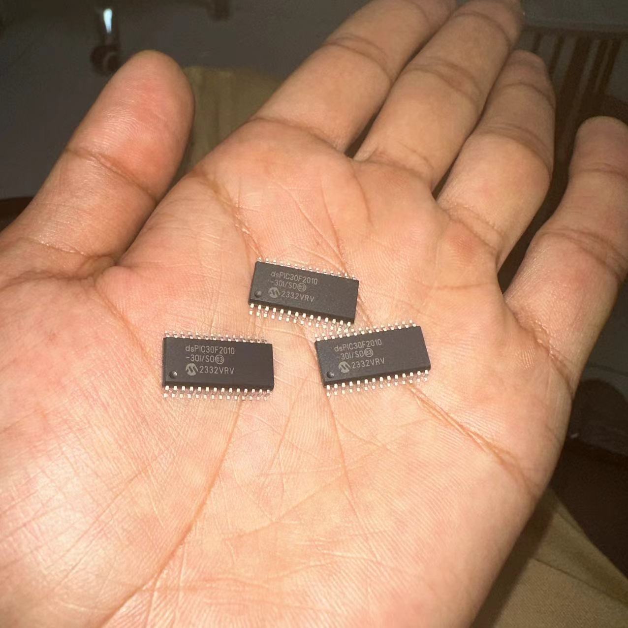 SMD DSPIC30F2010 - three black rectangular integrated circuit chips with silver pins, held in a person's open palm.