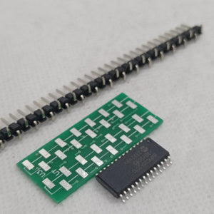 SMD DSPIC30F2010 - microcontroller chip, a green breakout adapter board, and a long strip of header pins arranged on a white surface.