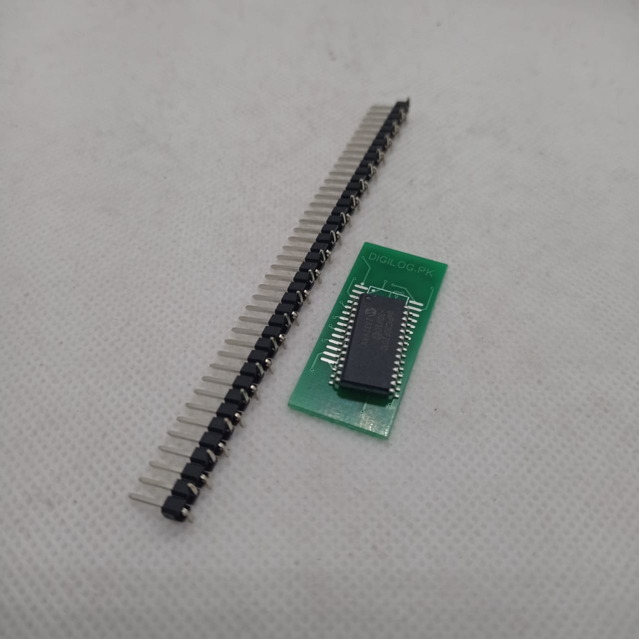 SMD DSPIC30F2010 - shown as a black integrated circuit on a small green breakout board next to a long strip of black male header pins.