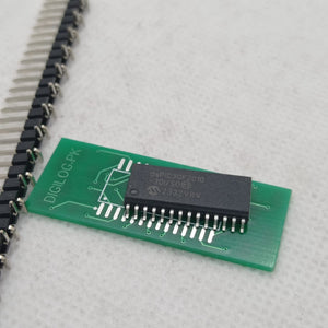 SMD DSPIC30F2010 - microcontroller chip mounted on a small green breakout board, positioned next to a strip of header pins.