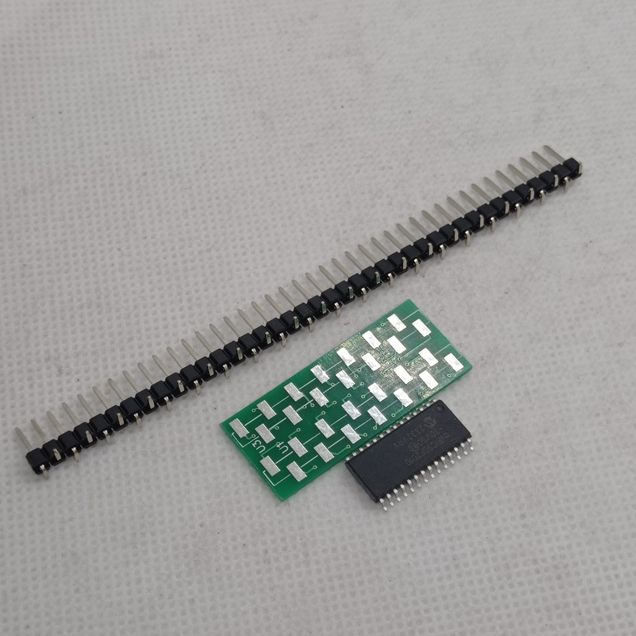 SMD DSPIC30F2010 - shown with a green breakout board and a long row of black male header pins on a white background.