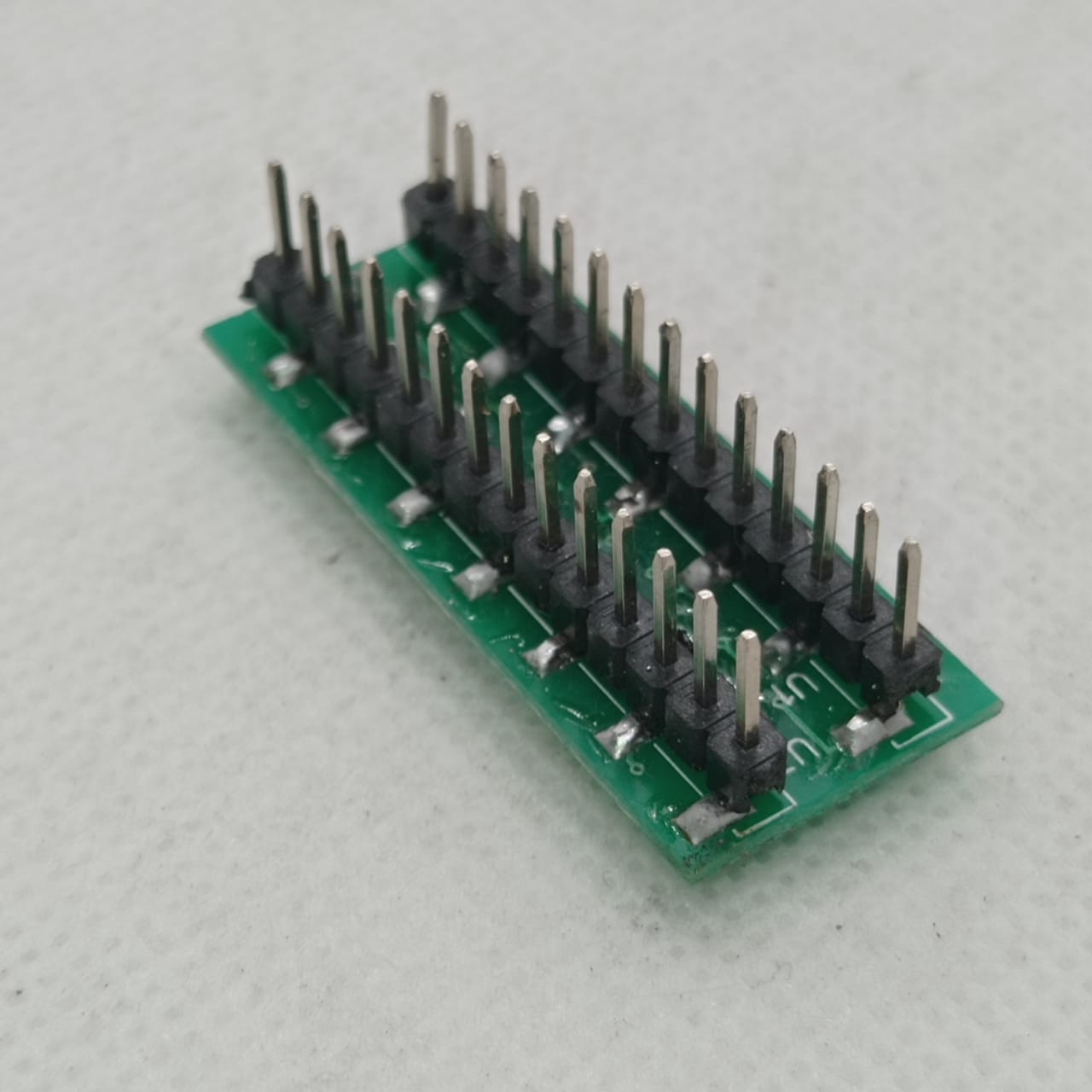 SMD DSPIC30F2010 - adapter board featuring a green rectangular PCB with two parallel rows of vertical male pin headers soldered onto the surface.