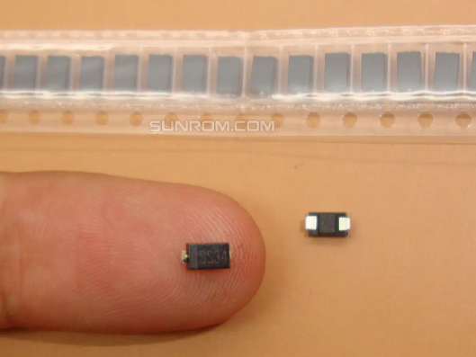 SMD Schottky Diode SS34 (1N5822) 3A/40V - shown as a small black rectangular component held on a finger next to another unit and a strip of identical components in packaging.